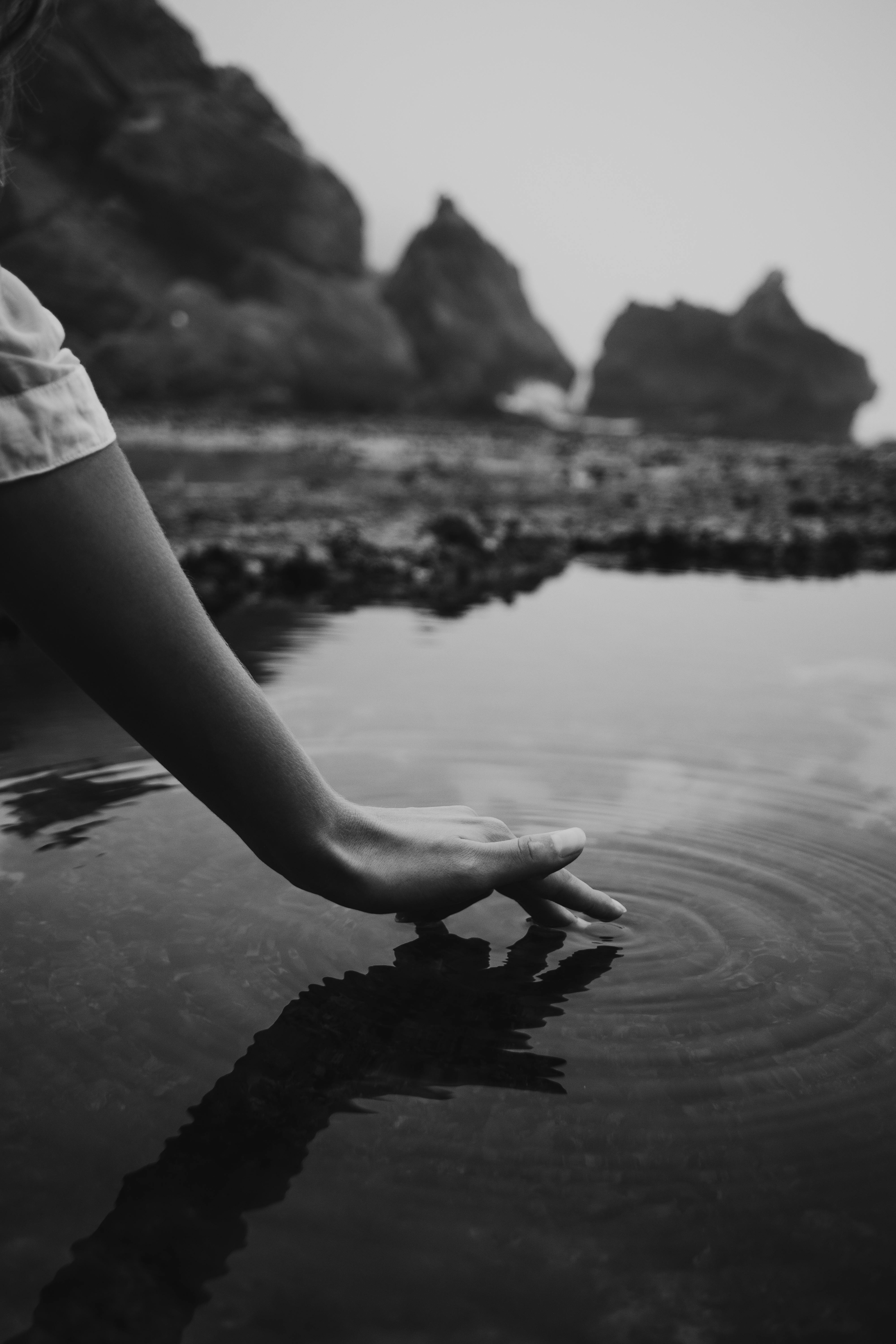 A close, black-and-white shot of a hand breaking the surface of still water.